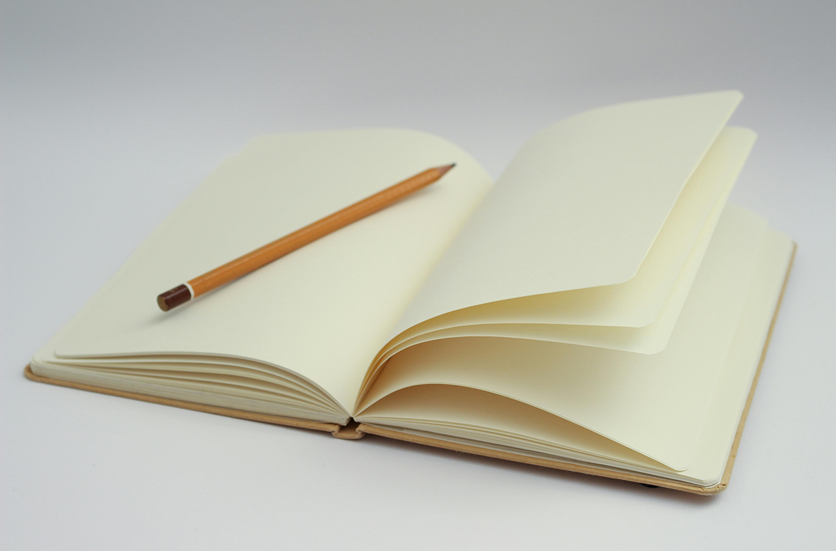 clean journal with blank white pages and yellow pencil resting on top on a white background